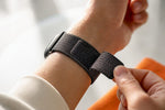 Die Hand schließt das textile Klettarmband passgenau.